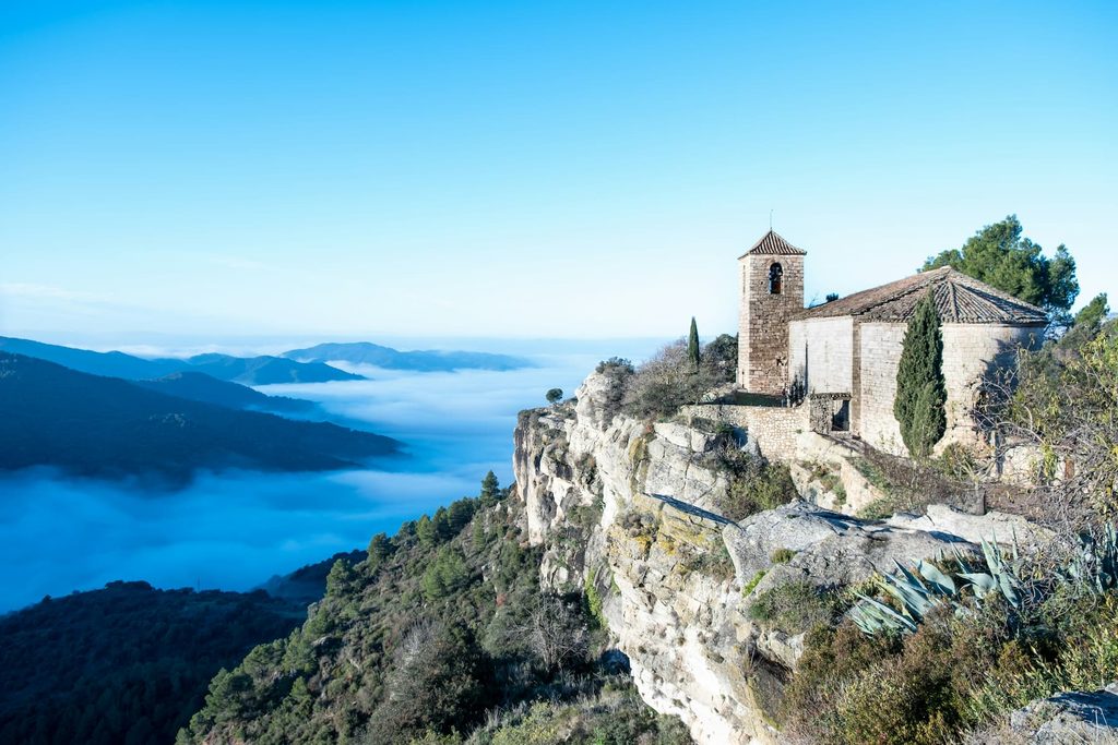 Iglesia románica de Santa María de Siurana sobre el cantil, con un mar de nubes en el valle