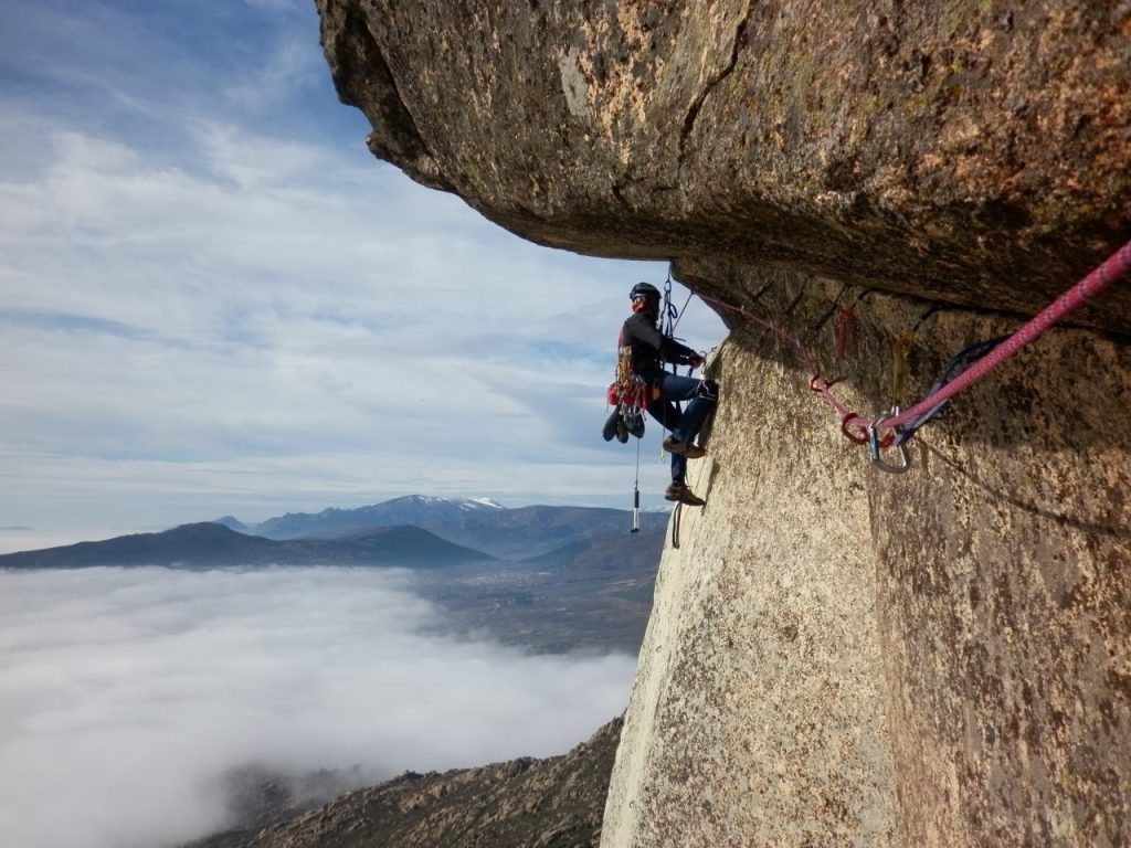 El guía Pablo Velasco en un largo de artificial bajo un techo de granito en La Cabrera, con un mar de nubes al fondo
