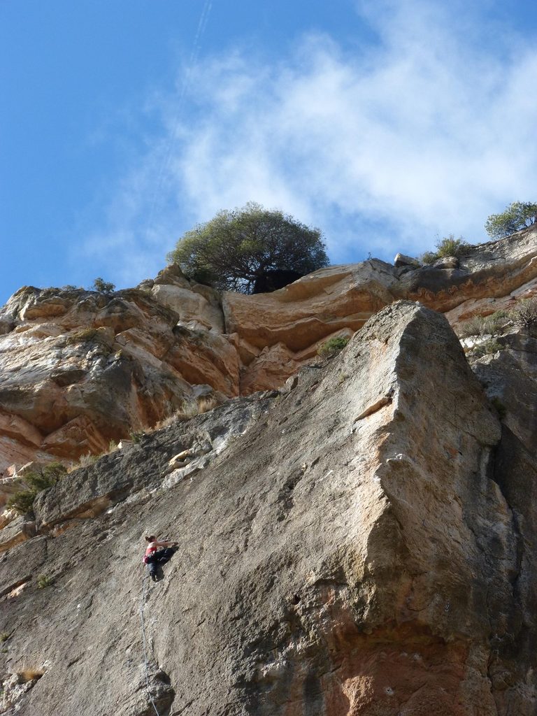 Escaladora en una placa vertical bajo un gran bloque de roca en Siurana