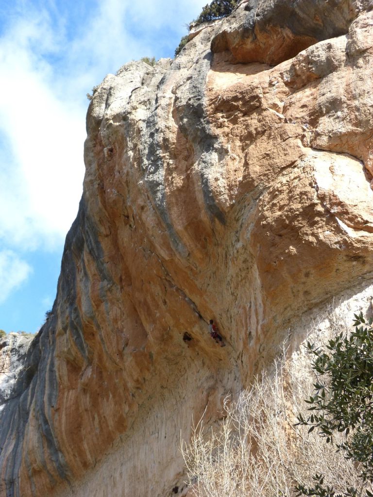 Escalador en un gran desplome de roca naranja en Siurana